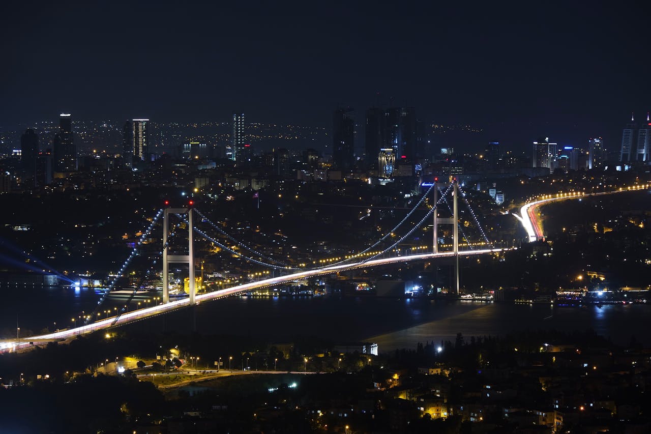 Capture of the iconic Bosphorus Bridge lit up against Istanbul's vibrant cityscape at night.